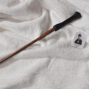 May include: A wooden wand with a dark handle and a small card with a picture of a person and the text "Harry Potter Wand" on a white towel.