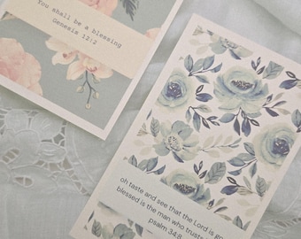 May include: Two floral greeting cards with inspirational quotes. One card features pink roses and the text "You shall be a blessing Genesis 12:2." The other card displays blue flowers and the text "oh taste and see that the Lord is good; blessed is the man who trusts in him. psalm 34:8."