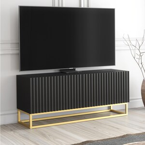 May include: A black TV stand with a ribbed front design and a gold-coloured base. The stand is positioned below a large, black flat-screen television. The stand is approximately 152 cm wide.