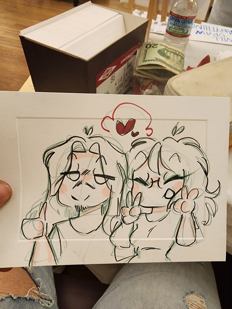 Peut inclure: Un croquis de deux personnages de dessins anim&eacute;s, l'un faisant un pouce lev&eacute; et l'autre un signe de paix. Le dessin est &agrave; l'encre noire et verte avec des accents rouges, dans un passe-partout blanc.