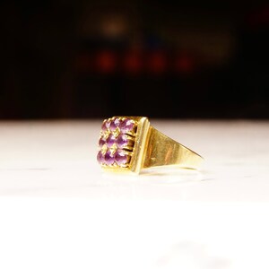 May include: A gold ring with a square-shaped setting featuring a cluster of purple gemstones.