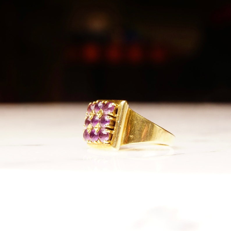 May include: A gold ring with a square-shaped setting featuring a cluster of purple gemstones.