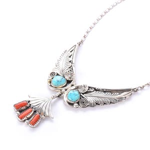 May include: A silver-toned necklace with a detailed feather design. The necklace features two turquoise stones and three coral-colored stones. The wingspan design is connected by a delicate chain, creating a unique and eye-catching piece of jewelry.