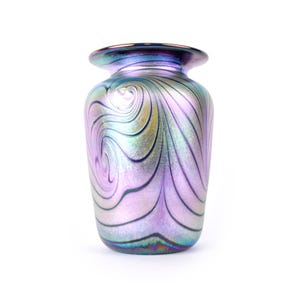 Puede incluir: Un jarrón decorativo de vidrio iridiscente con un diseño en espiral en tonos morados, plateados y verdes. El jarrón tiene un cuerpo redondeado y un borde ensanchado. Ideal para exhibir flores o como elemento decorativo.
