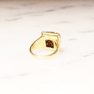 May include: A gold ring with a square-shaped setting filled with small purple gemstones.