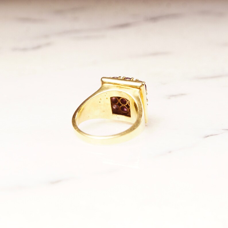 May include: A gold ring with a square-shaped setting filled with small purple gemstones.