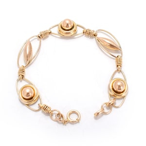 May include: A gold-toned bracelet with a delicate design. The bracelet features oval and circular links, with a ball-shaped accent in the center of each circular link. The links are connected by wire-wrapped sections, and the bracelet has a clasp closure.