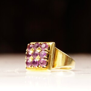 May include: A gold ring with a square-shaped setting featuring a cluster of purple gemstones.