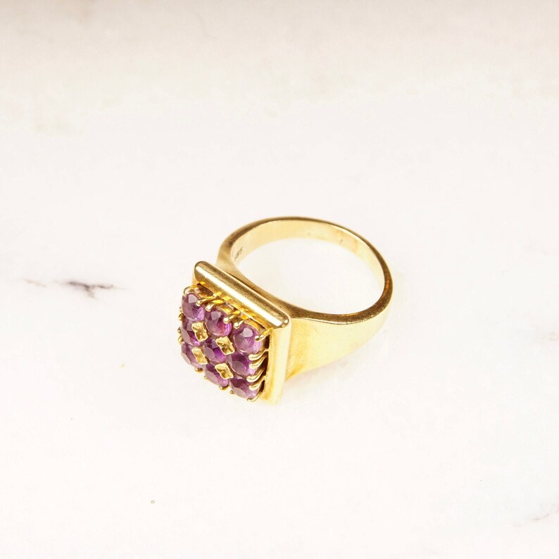 May include: A gold ring with a square-shaped setting featuring a cluster of purple gemstones.