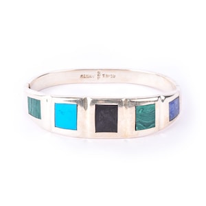 May include: Silver hinged bracelet with inlaid rectangular stones in turquoise, black, green, and blue. The bracelet is marked "MEXICO" and "TH-50". The bracelet is a piece of jewellery.