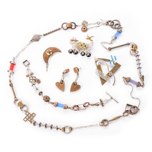 May include: An assortment of handcrafted jewelry pieces, including necklaces, earrings, and brooches. The collection features mixed metals, geometric shapes, and unique designs. Some pieces incorporate blue and red accents, and a small decorative animal.
