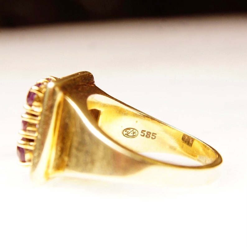 May include: A gold ring with a square-shaped setting featuring multiple small red gemstones. The ring is marked with the number "585" on the inside band.