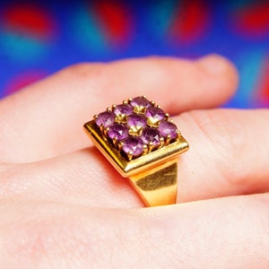 May include: A gold ring with a square-shaped setting featuring nine purple gemstones.