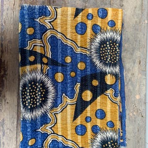 Può includere: Tessuto piegato con un motivo vibrante. Il design presenta una combinazione di forme blu, gialle e nere, tra cui grandi elementi floreali e pois. Il tessuto sembra essere trapuntato, con cuciture visibili.