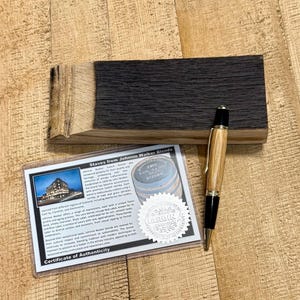 May include: A wooden pen with a light brown barrel and black accents rests on a dark wood block. A certificate of authenticity for Johnnie Walker Blends is also present, along with a wooden block.