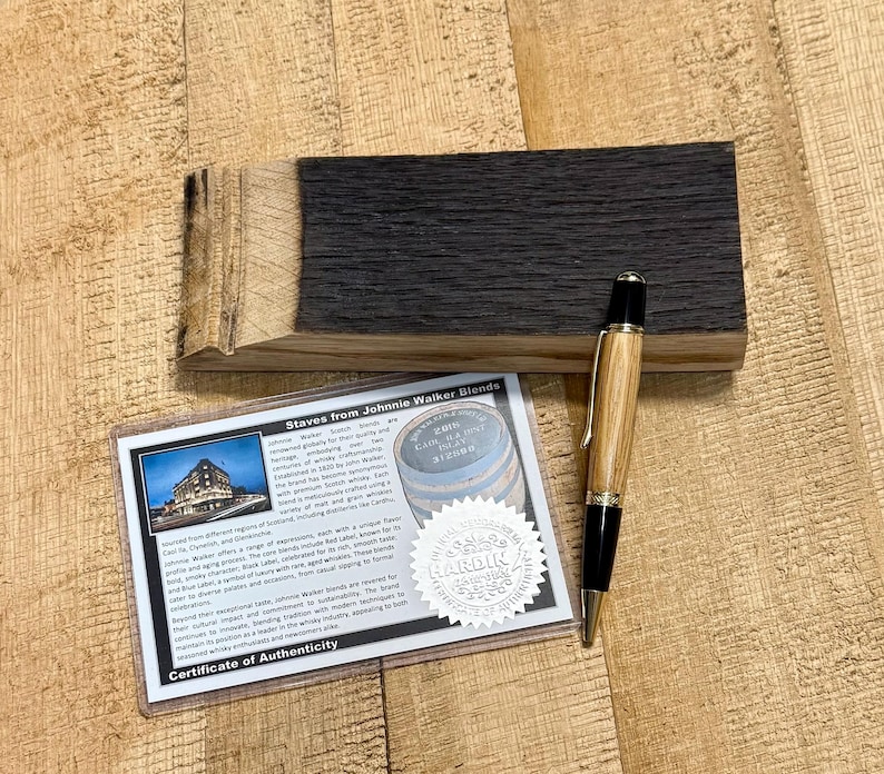 May include: A wooden pen with a light brown barrel and black accents rests on a dark wood block. A certificate of authenticity for Johnnie Walker Blends is also present, along with a wooden block.