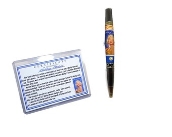 May include: A certificate of authenticity for a Marilyn Monroe pen. The certificate is in a clear plastic sleeve and features a black and white photo of Marilyn Monroe. The pen is black with a gold trim and features a color image of Marilyn Monroe on the barrel.