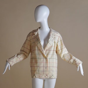 May include: Cream-coloured double-breasted blazer with a plaid pattern in red, green, and black. The blazer has long sleeves and a notched collar. The garment is displayed on a mannequin.