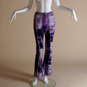 Puede incluir: Pantalones acampanados de color morado y blanco con estampado tie-dye en un maniquí blanco.