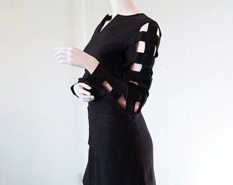 May include: A black mini dress with long sleeves featuring a unique cut-out design on the sleeves. The dress has a simple, fitted silhouette.