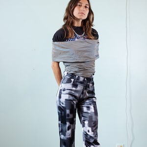 May include: A person wearing black and white patterned trousers with a silver top and a black t-shirt with a graphic print.