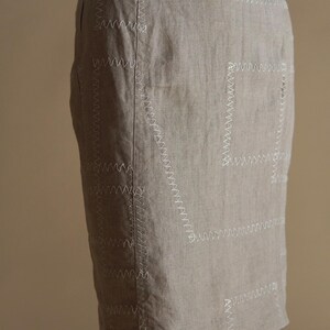 May include: A beige linen skirt with decorative white stitching in a geometric pattern.