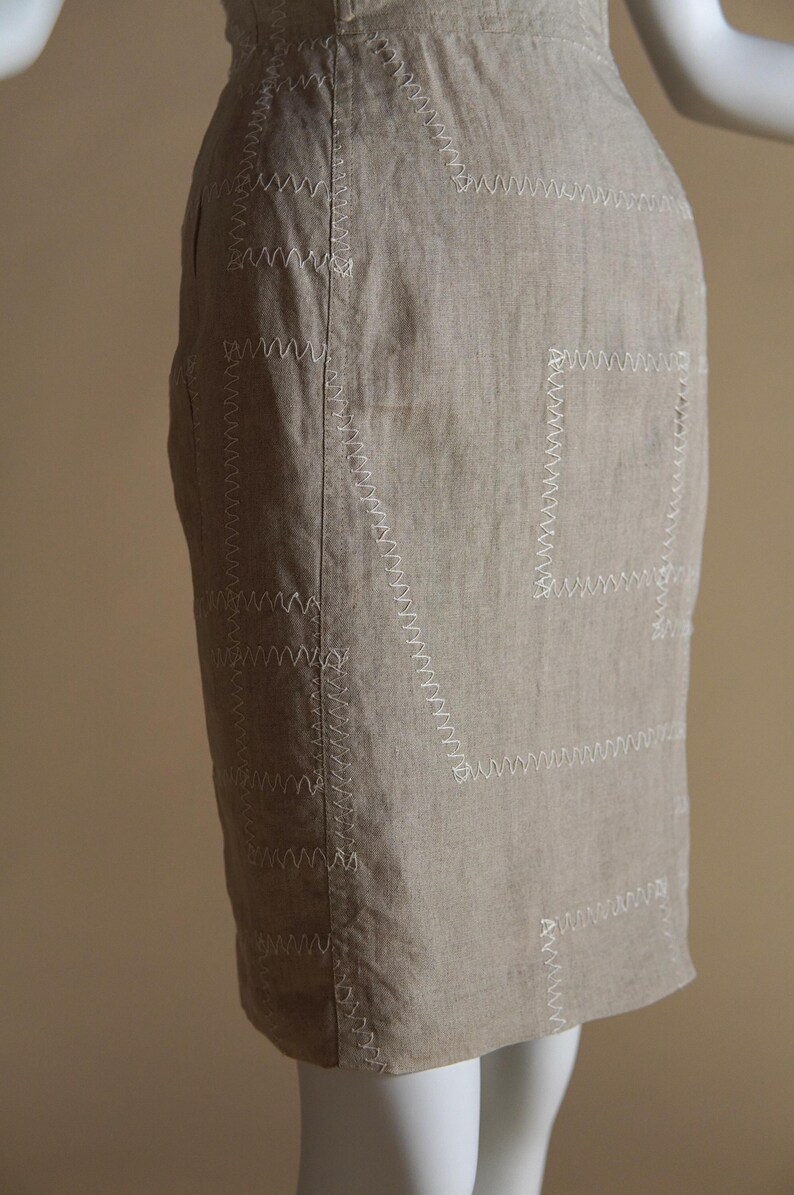 May include: A beige linen skirt with decorative white stitching in a geometric pattern.