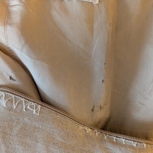 May include: A beige linen garment with a label that reads "Patrick Kelly Paris" and "Made in France". The garment has decorative stitching around the edges.