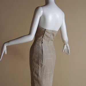May include: A beige strapless dress with a fitted silhouette and a geometric pattern. The dress is made of a textured fabric and has a zip closure at the back.