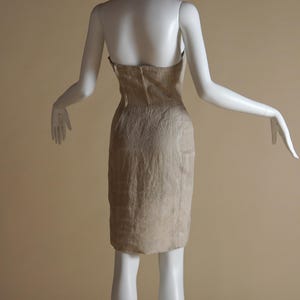May include: A strapless beige dress with a geometric pattern. The dress is fitted and has a straight skirt.