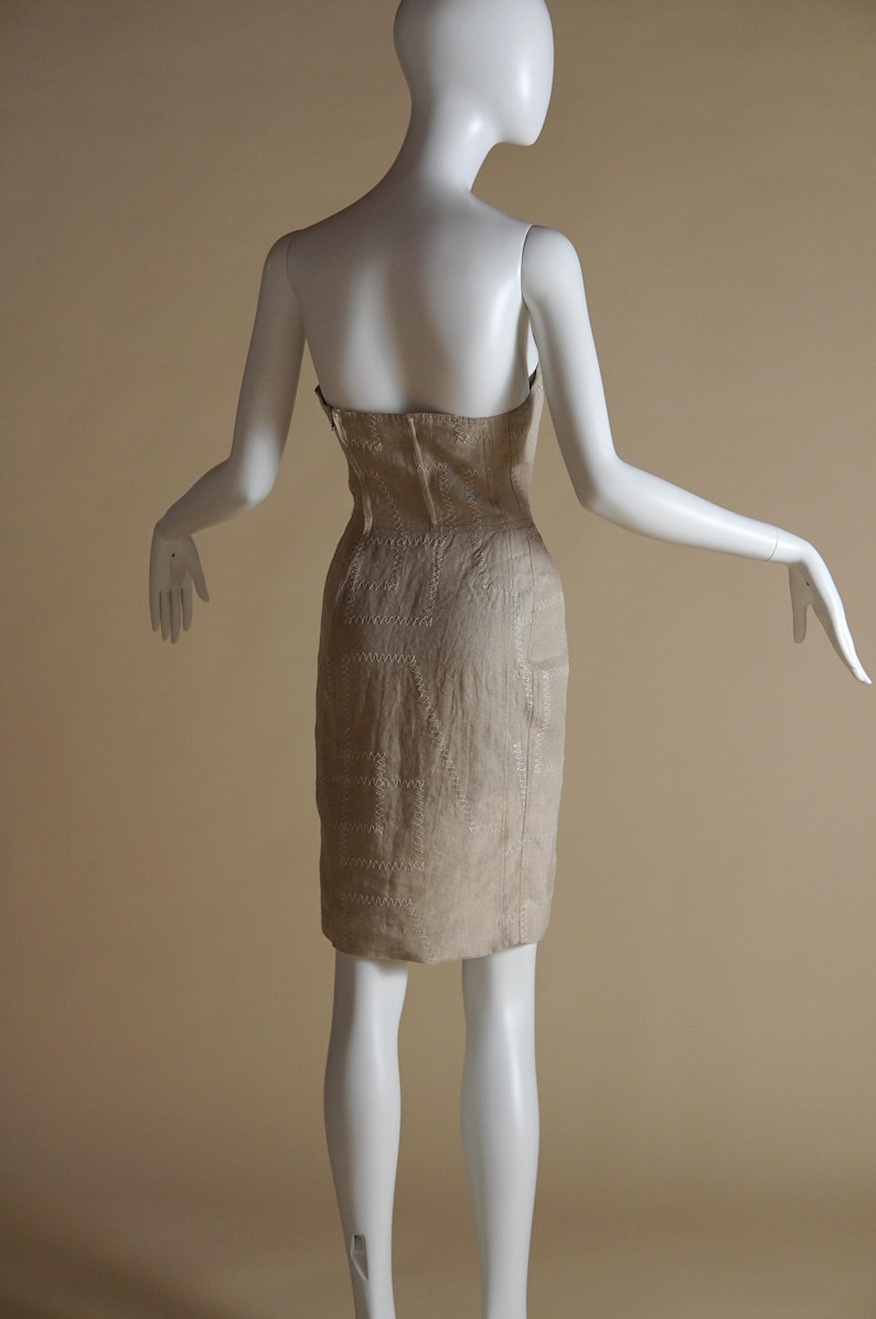 May include: A strapless beige dress with a geometric pattern. The dress is fitted and has a straight skirt.