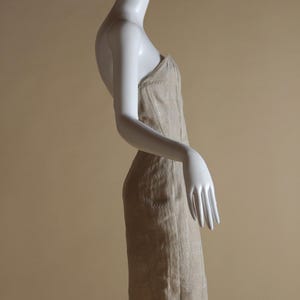 May include: A strapless dress with a beige and white embroidered pattern. The dress is fitted and has a straight skirt.