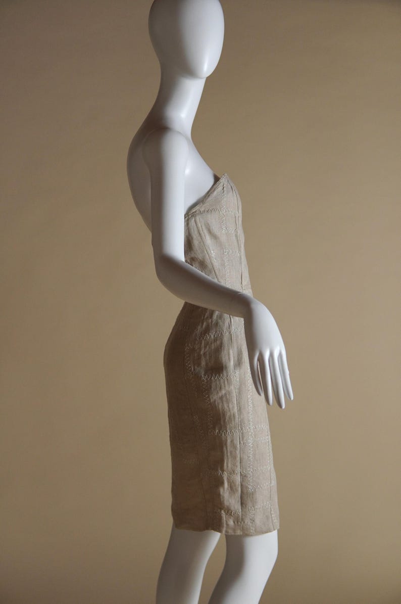 May include: A strapless dress with a beige and white embroidered pattern. The dress is fitted and has a straight skirt.