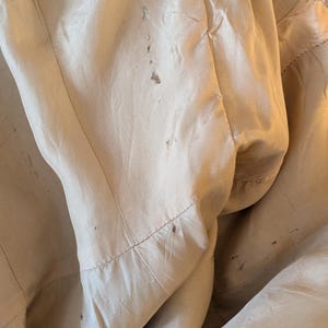 May include: The inside of a beige jacket with a satin lining. The lining has several small brown stains.