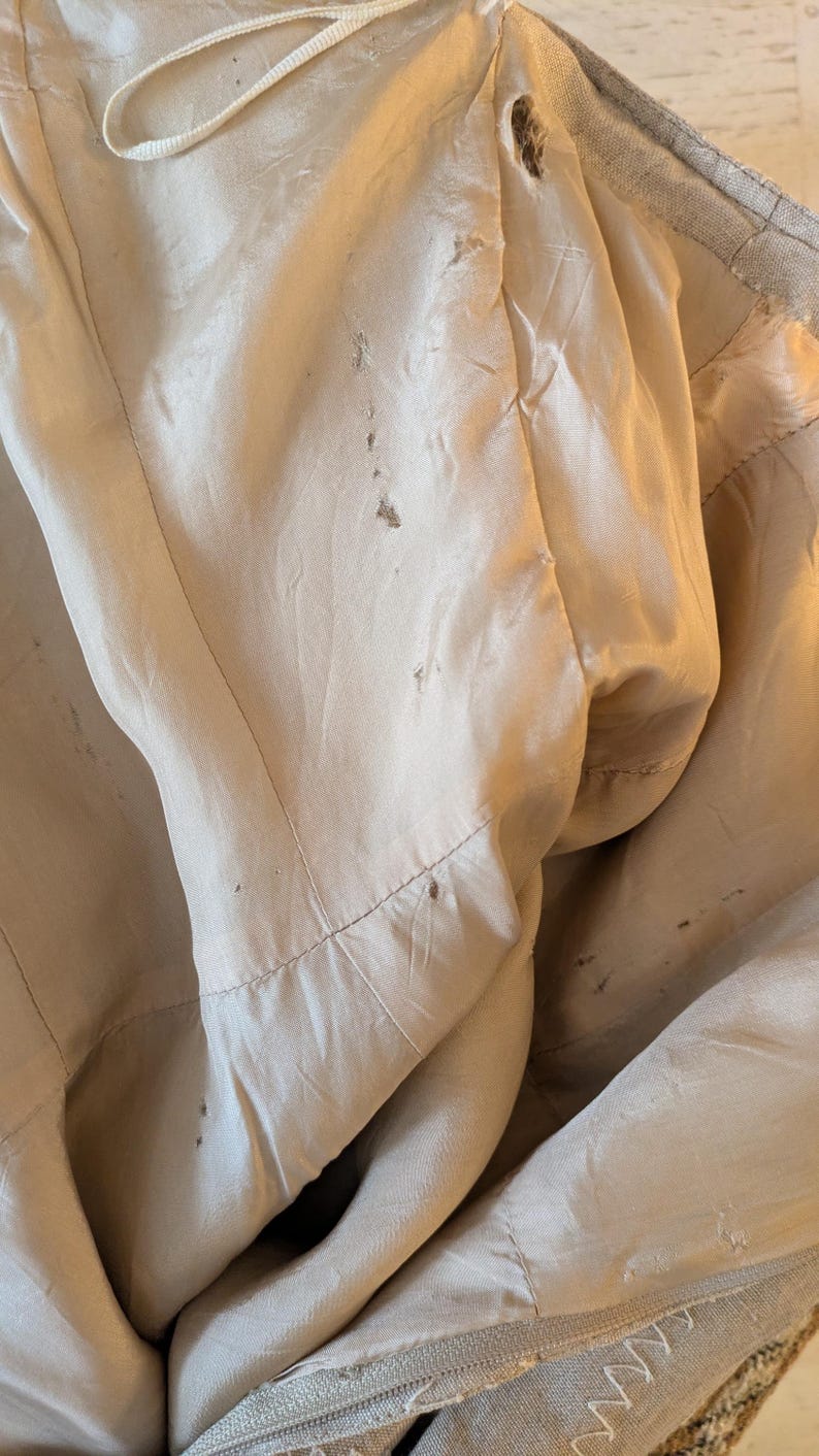 May include: The inside of a beige jacket with a satin lining. The lining has several small brown stains.