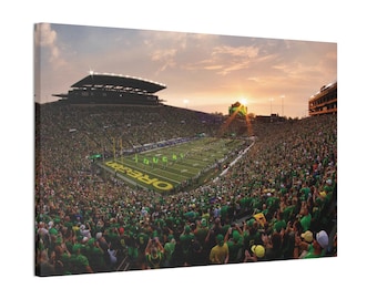Könnte beinhalten: Leinwanddruck eines überfüllten Fußballstadions bei Sonnenuntergang. Das grüne Spielfeld zeigt das Wort "OREGON" in Gelb. Die Tribünen sind mit grün gekleideten Fans gefüllt. Der Himmel ist eine Mischung aus Orange und Gelb.