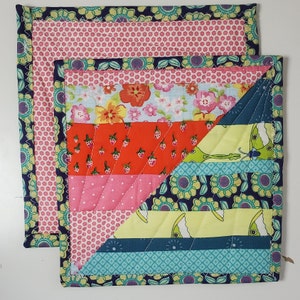 Puede incluir: Dos salvamanteles cuadrados acolchados hechos a mano. Uno presenta un estampado floral y de fresas, el otro un estampado floral y de lunares. Los bordes están acabados con una tela floral azul oscuro y costuras blancas.