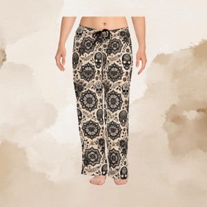 Puede incluir: Pantalones de pijama color crema con un estampado floral y calaveras en negro. Los pantalones tienen cintura con cord&oacute;n y un ajuste relajado. El dise&ntilde;o incluye calaveras estilizadas, flores y otros elementos decorativos.