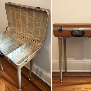 May include: A vintage suitcase repurposed as a side table with wooden legs. The suitcase is brown with a silver latch and handle. The inside of the suitcase is lined with pages from a book.