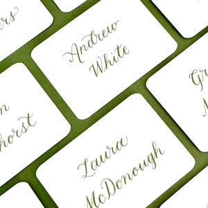 May include: White place cards with green borders and calligraphy names, including Andrew White, Laura McDonough, and others.