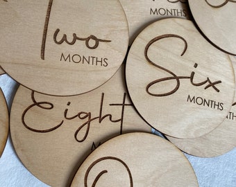 Può includere: Set di dischi in legno per pietre miliari del bambino con numeri e frasi incisi, tra cui "Una settimana", "Due mesi", "Tre mesi", "Sei mesi" e "Otto mesi".
