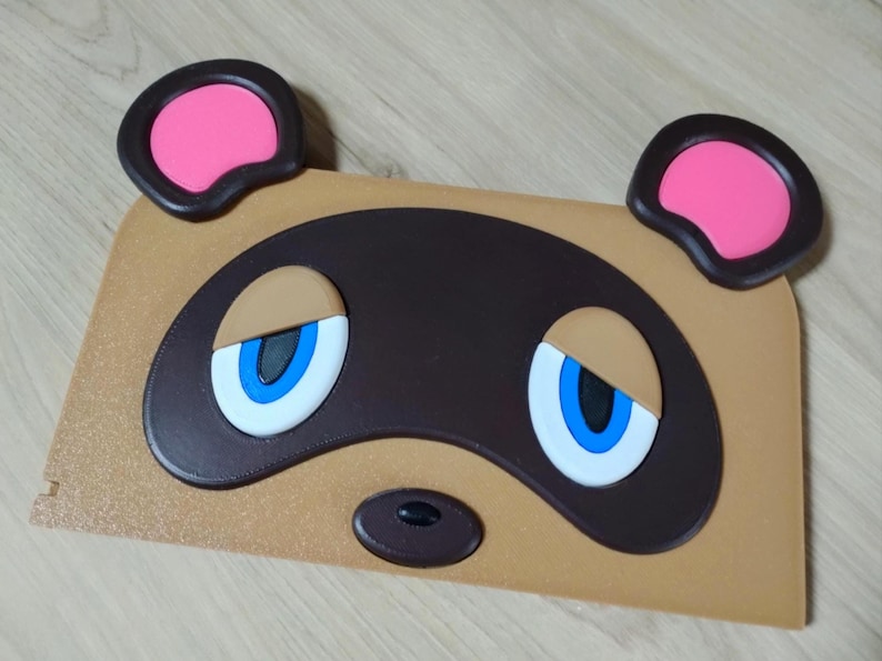 May include: A tan-colored, rectangular item featuring a cartoon face with large blue eyes, a black nose, and two pink-filled ears. The design is reminiscent of a popular video game character.