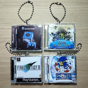 Peut inclure: Quatre porte-clés en acrylique transparent avec des mini-boîtiers de jeux. Les boîtiers présentent des titres de jeux vidéo emblématiques : GameCube, The Legend of Zelda: The Wind Waker, Final Fantasy VII et Sonic Adventure. Chaque porte-clés comprend une chaîne à billes argentée.