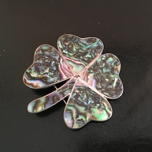 Op de afbeelding: Een zilveren vierbladige klaver broche met een inleg van groene, blauwe en paarse abalone schelp.