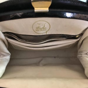 May include: Interior view of a vintage black handbag with a gold clasp. The inside is cream-colored with multiple compartments and a zippered pocket. A gold emblem is visible, with the text "Made in Poland".