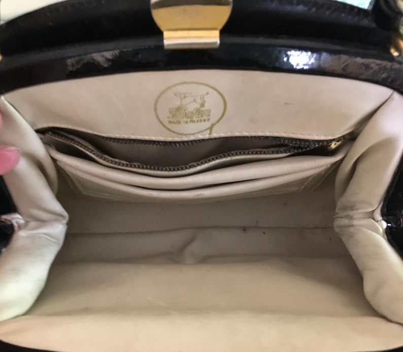 May include: Interior view of a vintage black handbag with a gold clasp. The inside is cream-colored with multiple compartments and a zippered pocket. A gold emblem is visible, with the text "Made in Poland".