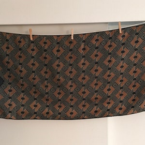 May include: A black and brown geometric patterned scarf with a black border. The scarf is hanging on a clothesline with wooden clothespins.
