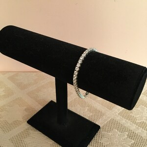 May include: A silver bracelet with clear cubic zirconia stones set in a pave setting. The bracelet is displayed on a black velvet jewellery stand.