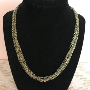 May include: A gold-toned multi-strand chain necklace on a black velvet display stand.
