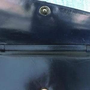 May include: A navy blue leather handbag with a flap closure and a gold-colored clasp. The interior features a strap and a smooth, glossy finish. The bag is open, revealing the inside.
